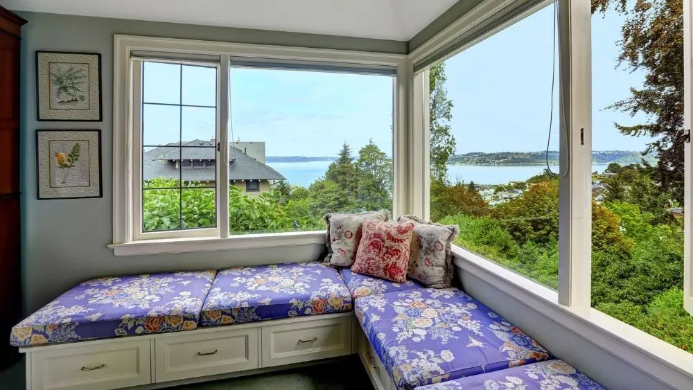 A corner bench in a bay window with floral cushions overlooking a scenic view.