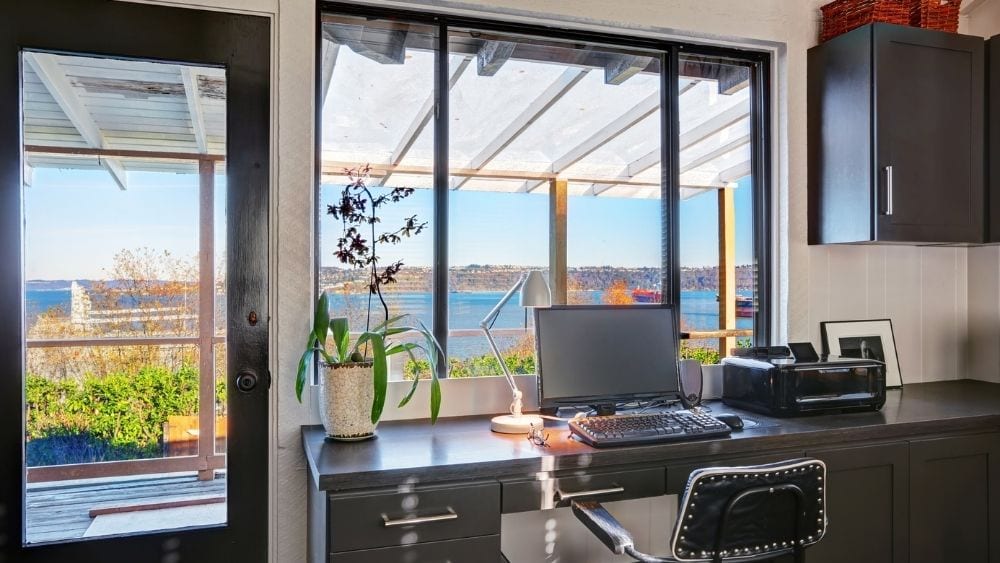 Office desk in front of windows and a glass door, letting in sunlight and showing a natural view.
