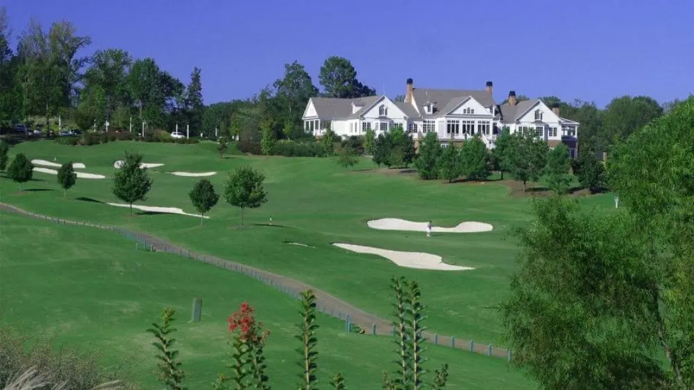 A country club surrounded by a well-maintained golf course and trees on a clear day.