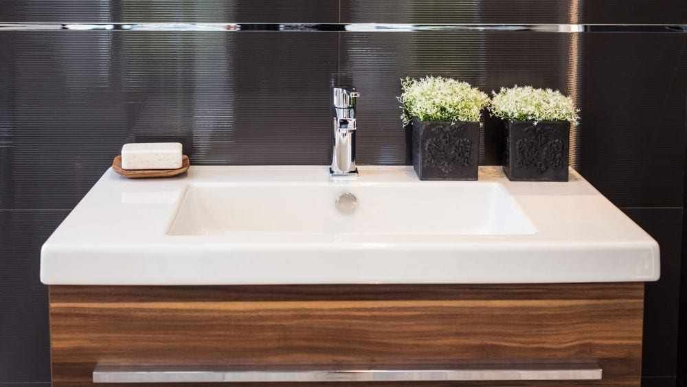 A modern bathroom sink with a dark wood countertop and black walls with inset lighting.