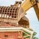 An excavator demolishing a home with a Spanish-style roof.