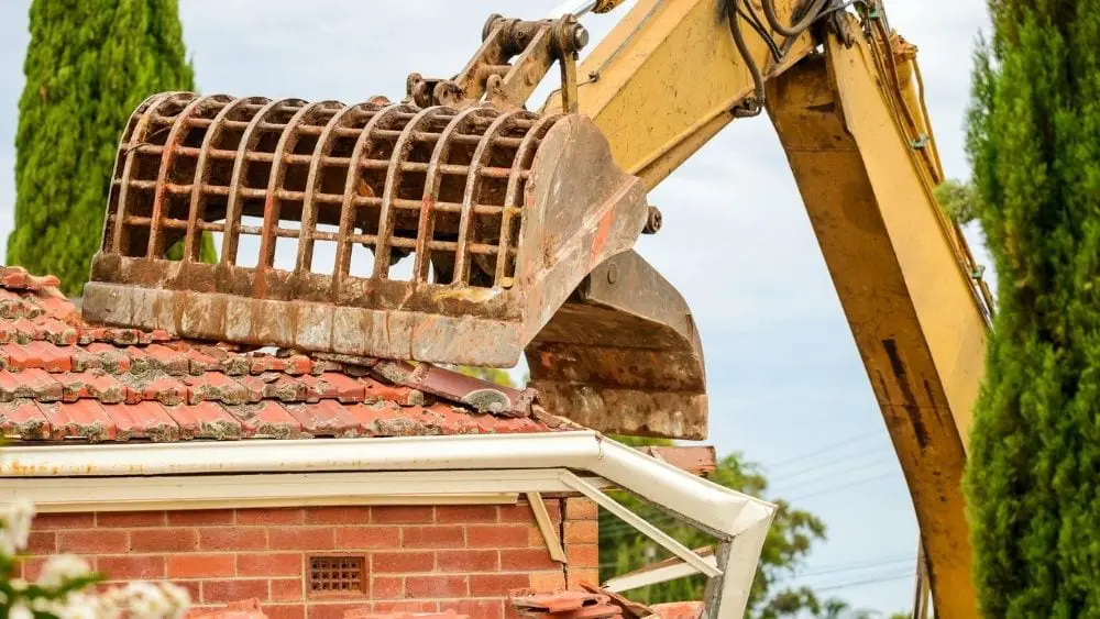 An excavator demolishing a home with a Spanish-style roof.