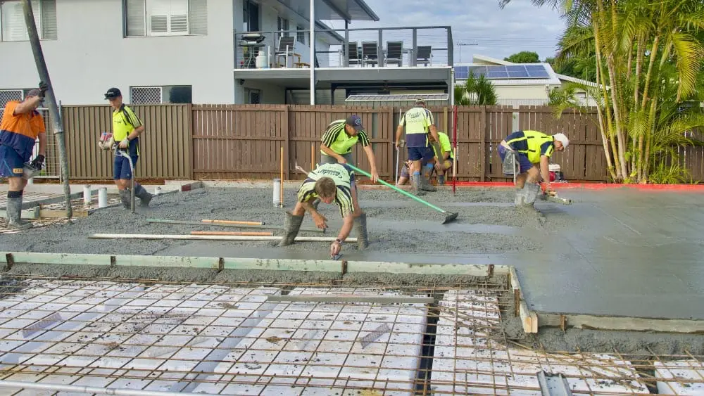 Construction workers spread and smooth concrete for a slab home foundation.