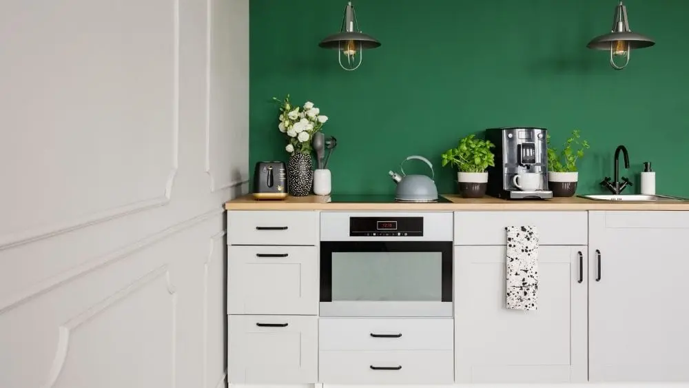 A kitchen with white cabinets and a green wall, and a coffee station set up by the sink.