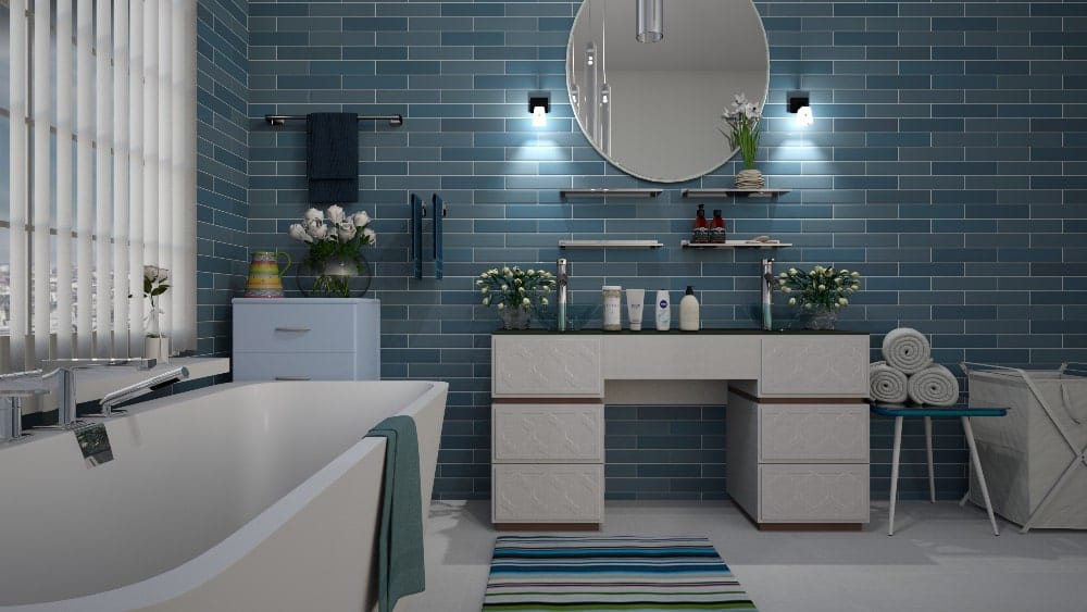Bathroom featuring standalone white tub on left and dual vanity at center along a blue-tile wall with a round mirror above the vanity