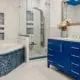 Bathroom featuring tub on left surrounding by blue tile, a glass-enclosed shower, center, and royal blue vanity at right