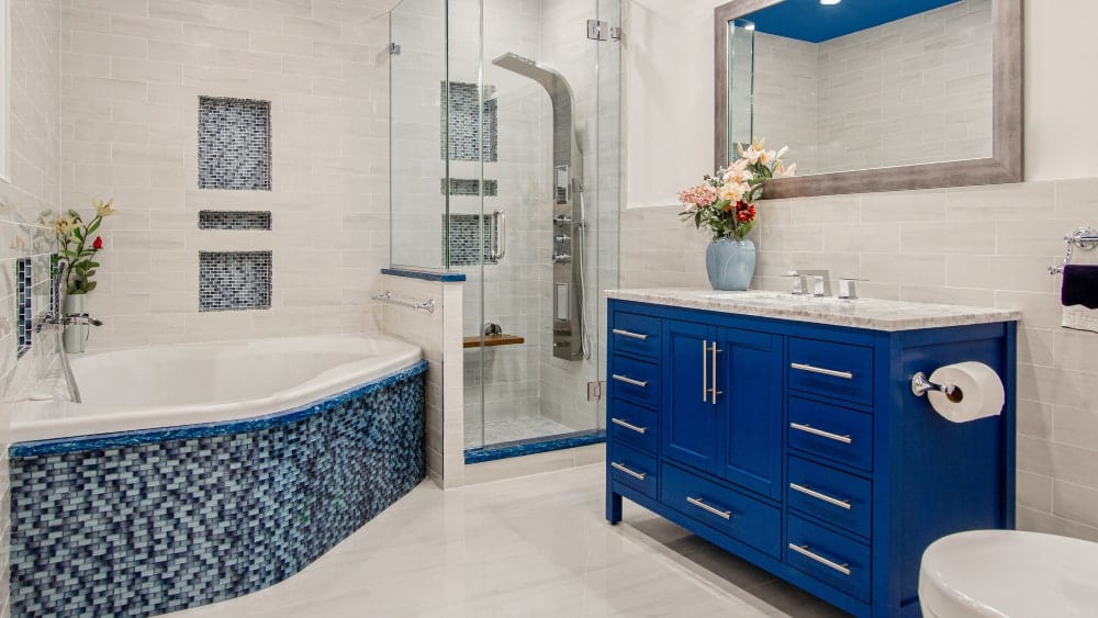 Bathroom featuring tub on left surrounding by blue tile, a glass-enclosed shower, center, and royal blue vanity at right