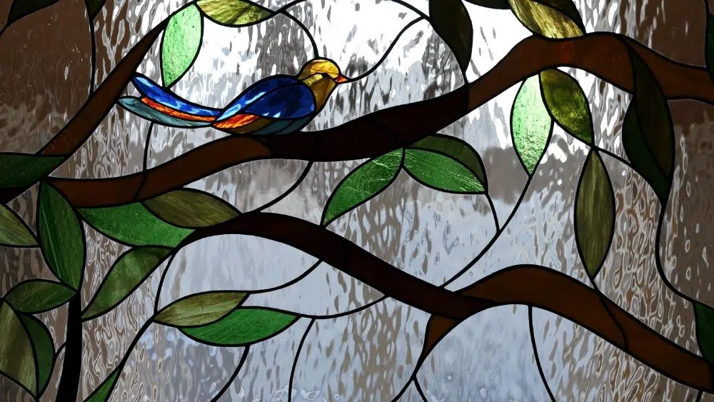 A stained glass window with a bird on a branch.