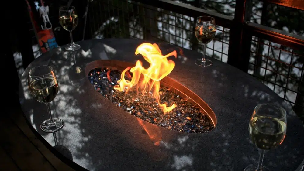 A lit fire glass pit with wine glasses surrounding it.