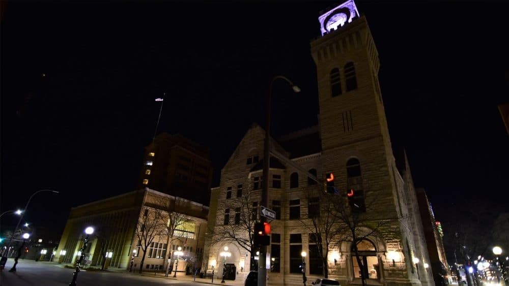 Angled view from below of a large stone building with a clocktower. The background is dark, and the clockface is lit up.