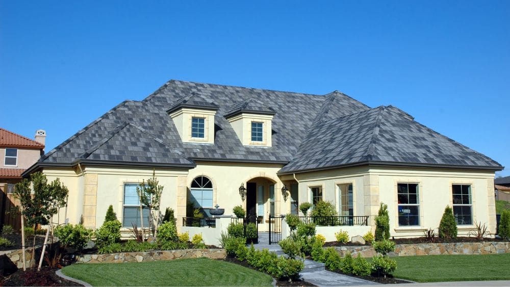 A custom home with off-white exterior walls and a grey and black slate roof.