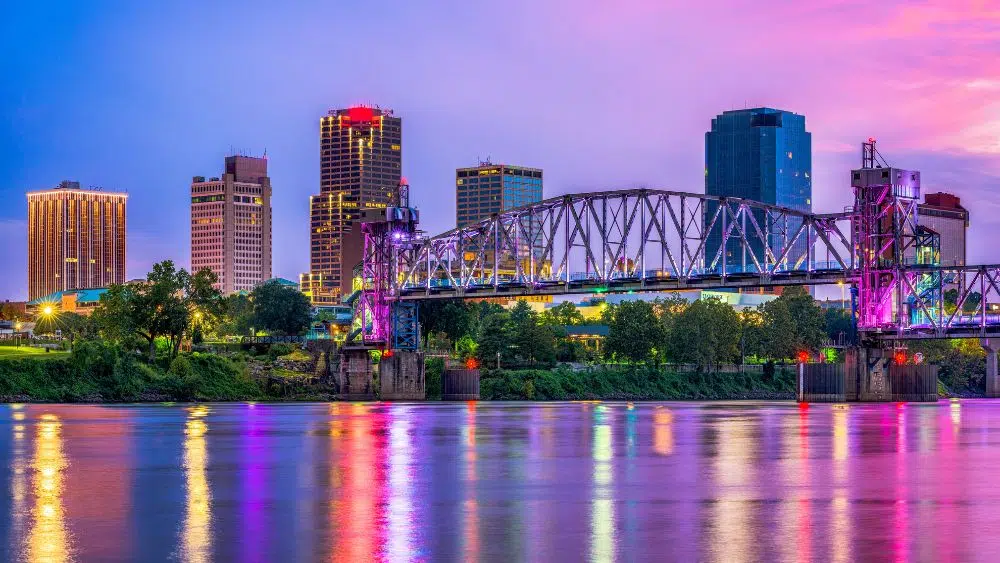 City skyline along a river. There are five major buildings and a steel bridge, and the image is mostly in pinks and blues.