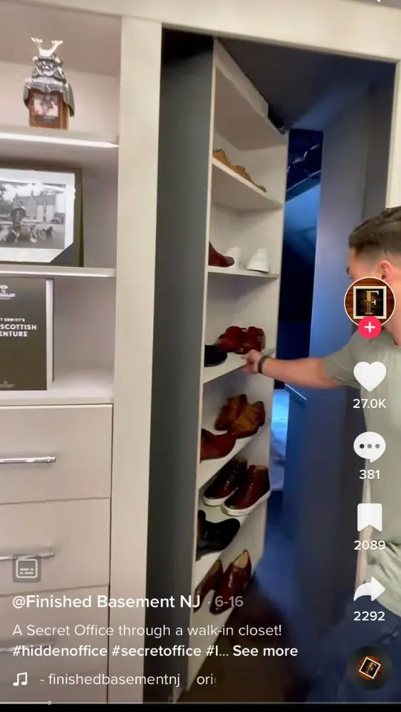 Screenshot of @finishedbasementnj's TikTok video showing a person pushing a shelf of shoes inward to reveal a hidden office space.