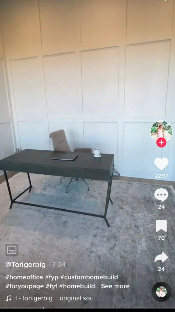 Screenshot of @torigerbig's TikTok video showing a grey desk against a white wall with wainscoting panels from floor-to-ceiling.