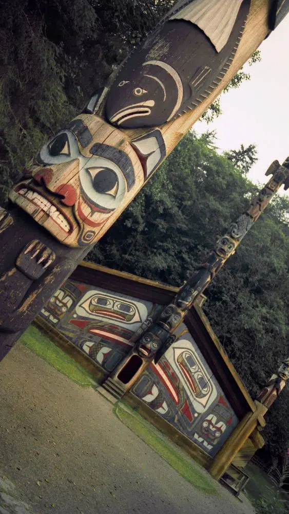 Angled photo of a traditional totem pole in front of a historic home.