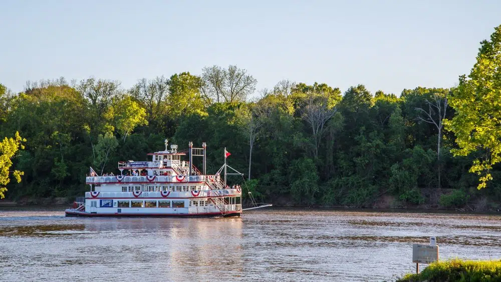 A white steamboat cruises along a quiet river.