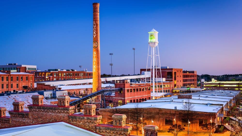 Large smokestack that reads "Lucky Strike" next to a water tower. Both are surrounded by smaller brick buildings.
