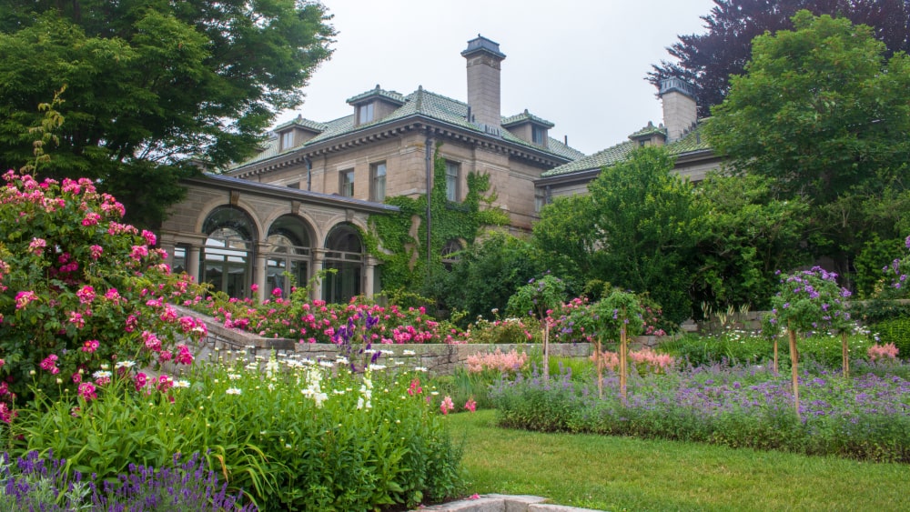 view of formal gardens, with pink, white, and purple blossoms, at Harkness Memorial State Park, with view of the Edward and Mary Harkness mansion in the background