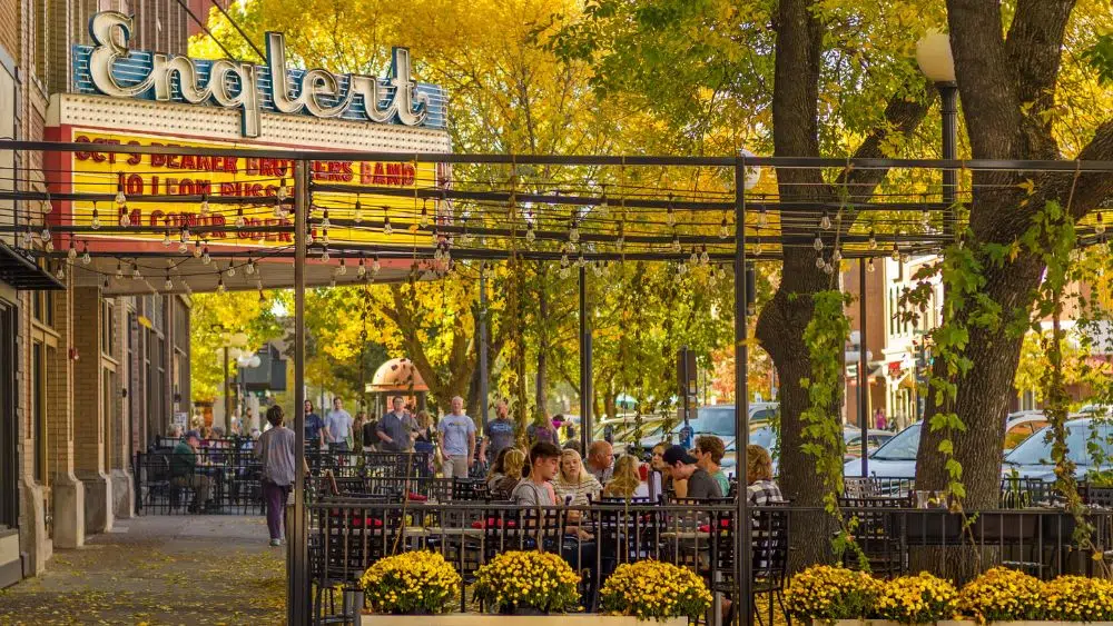 A fall day with people sitting outside at a cafe. A light-up sign in the upper left of the image reads "Englert." Below that is a marquee sign with red letters.