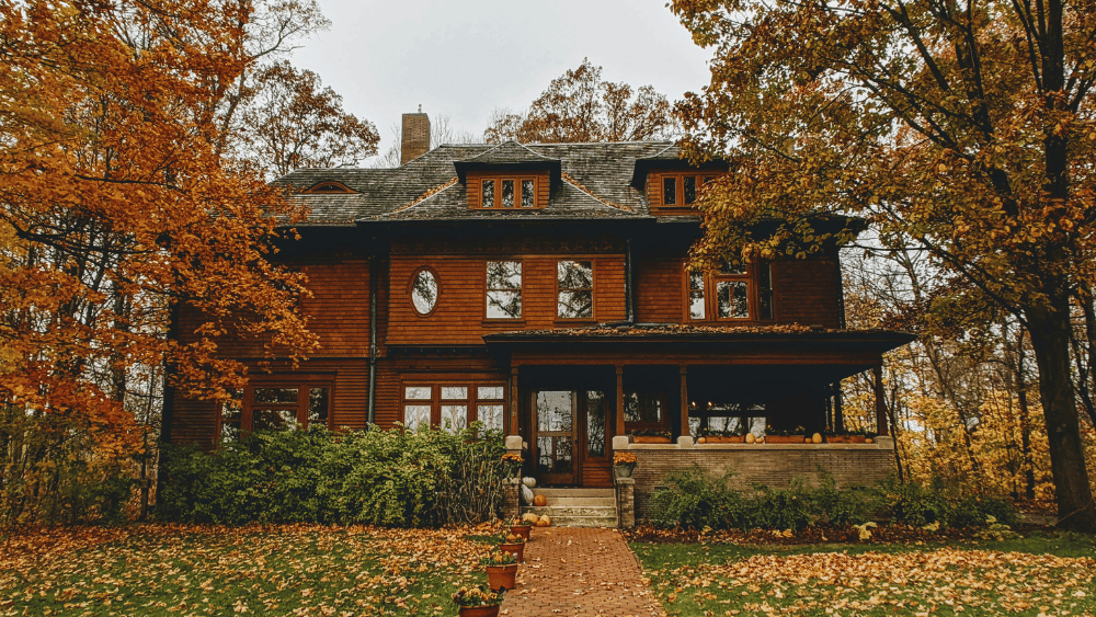 The Oakhurst House, in Muncie, Indiana, a large home with windows and brown wood siding. Trees and green grass with autumn leaves.