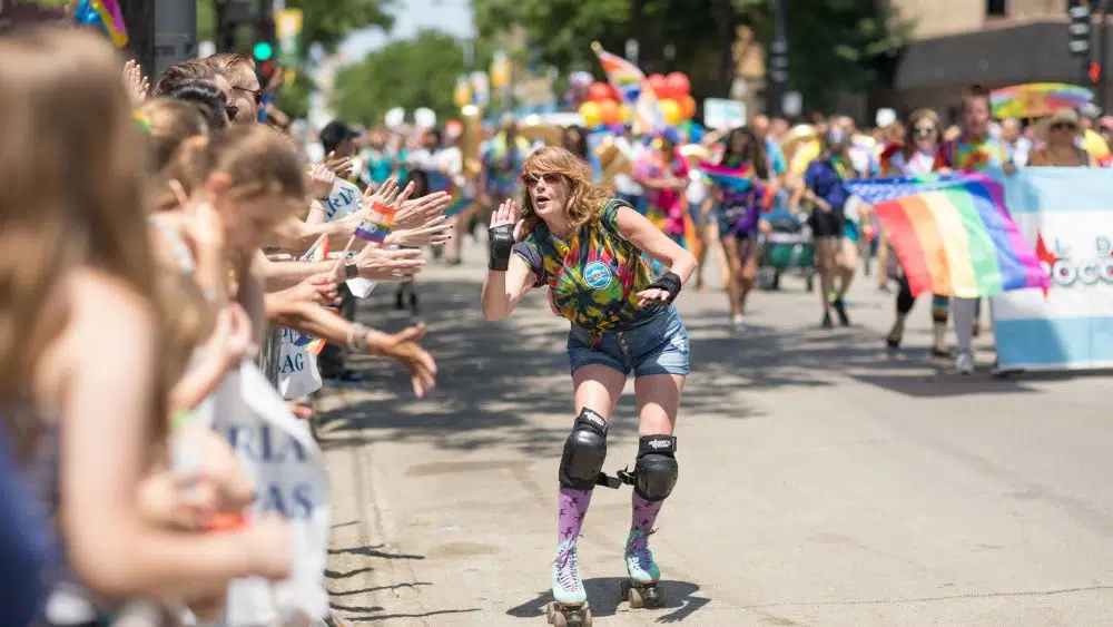 A feminine person on roller skates high-fiving parade watchers during an LGBTQIA+ Pride Parade.
