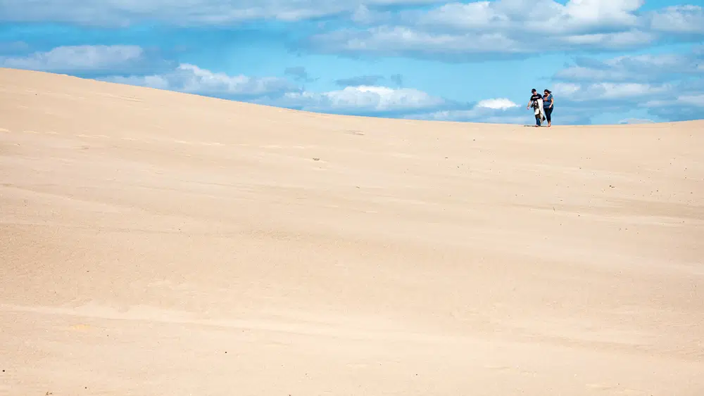 Daytime view of sandy dunes with two figures walking across the sand in the background at Silver Lake State Park, Michigan.