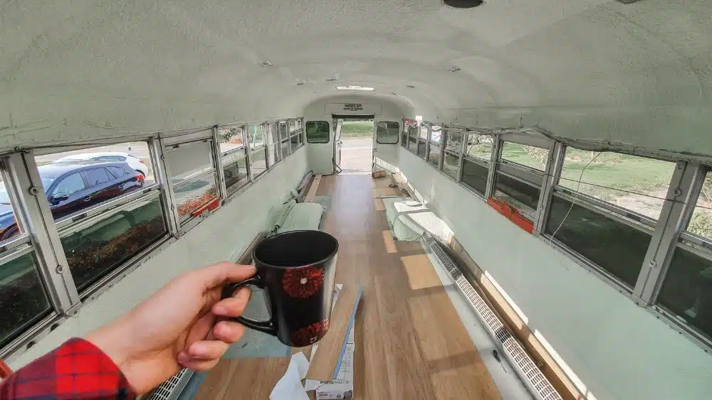 The inside of a school bus with the seats removed, the walls painted, and vinyl flooring being added.