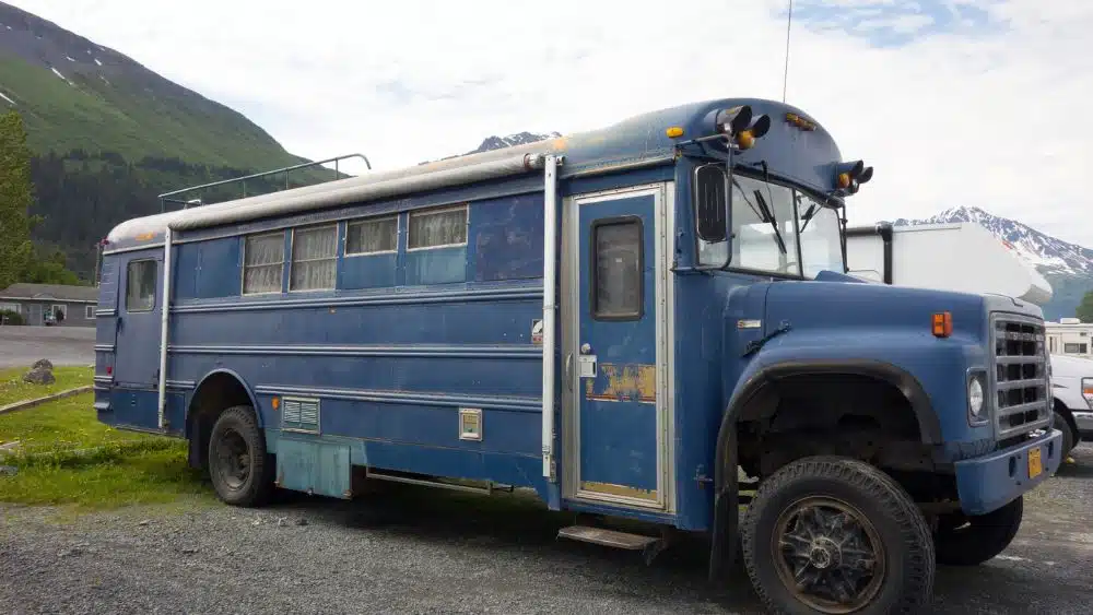 A converted school bus painted blue with an RV door and curtains in the windows.