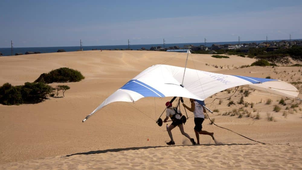 A person anchored into a hanglider, preparing to takeoff over sand dunes.