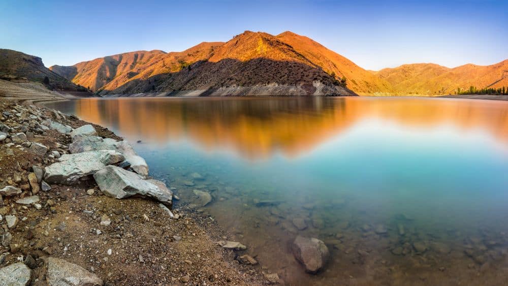 A mountain bathed in golden sunlight reflected on a lake.
