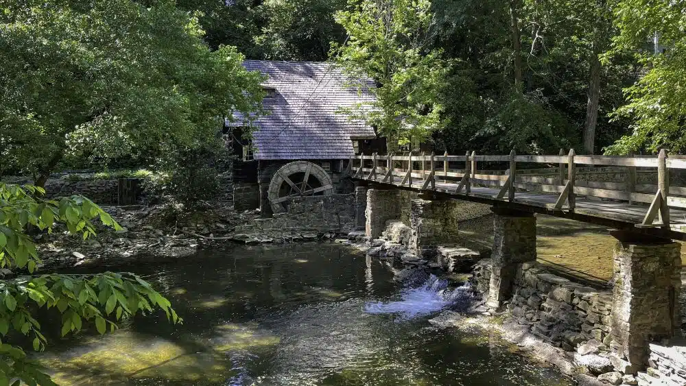 An old water mill behind a bridge crossing over a river.