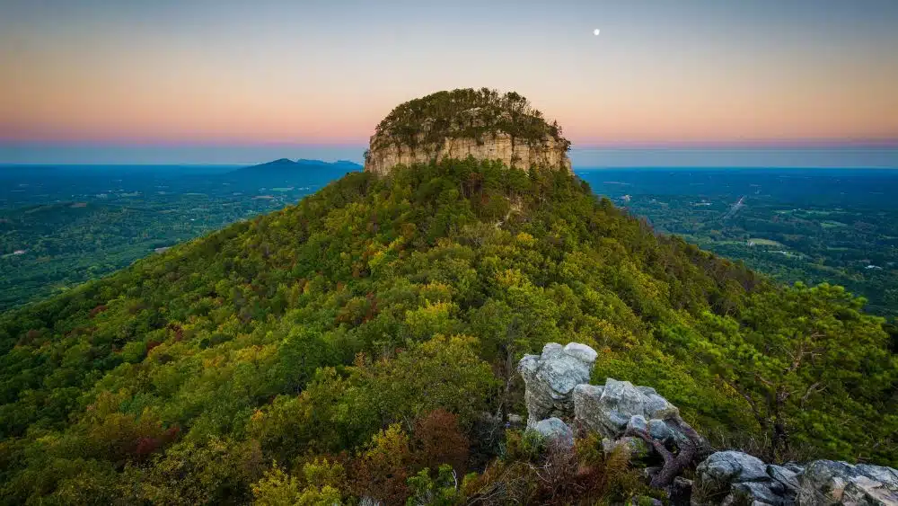 A mountain covered in trees. The peak is a cylindrical rock formation with a rounded top.