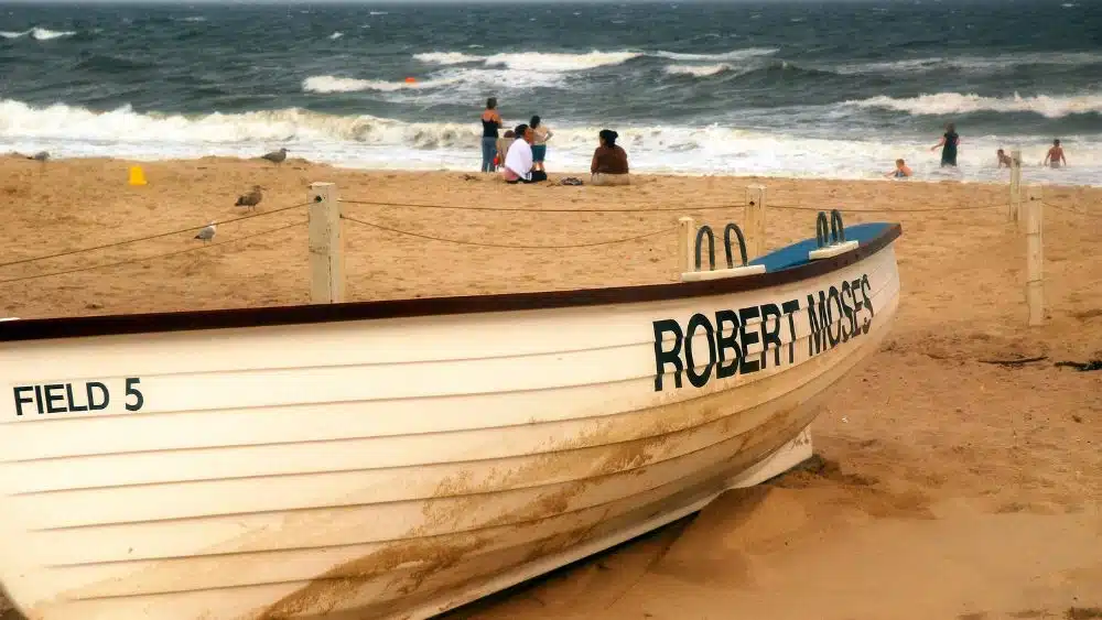 A sandy beach with a white boat that has "Robert Moses" painted on the side.