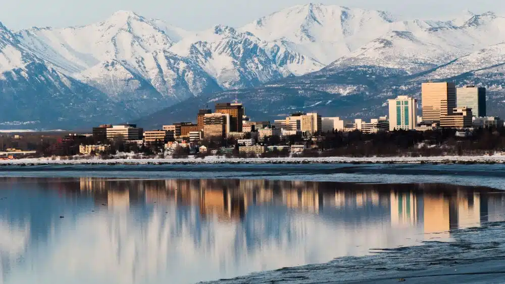 Askyline reflected in a body of water with a snow-capped mountain range in the background.