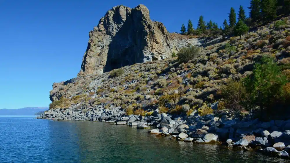 Rocky shore of a lake with a large, free-standing cave carved into a rock.
