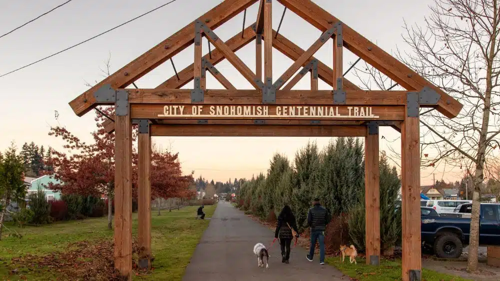 A wooden A-frame structure over a paved path. Letters on the structure read, "City of Snohomish Centennial Trail."