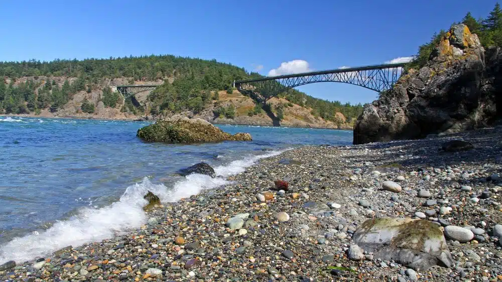 Shore covered in stones. In the distance is a long bridge spaning a river between two islands.