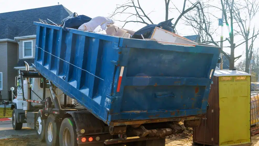 blue dumpster full of home demolition debris being loaded onto truck for removal