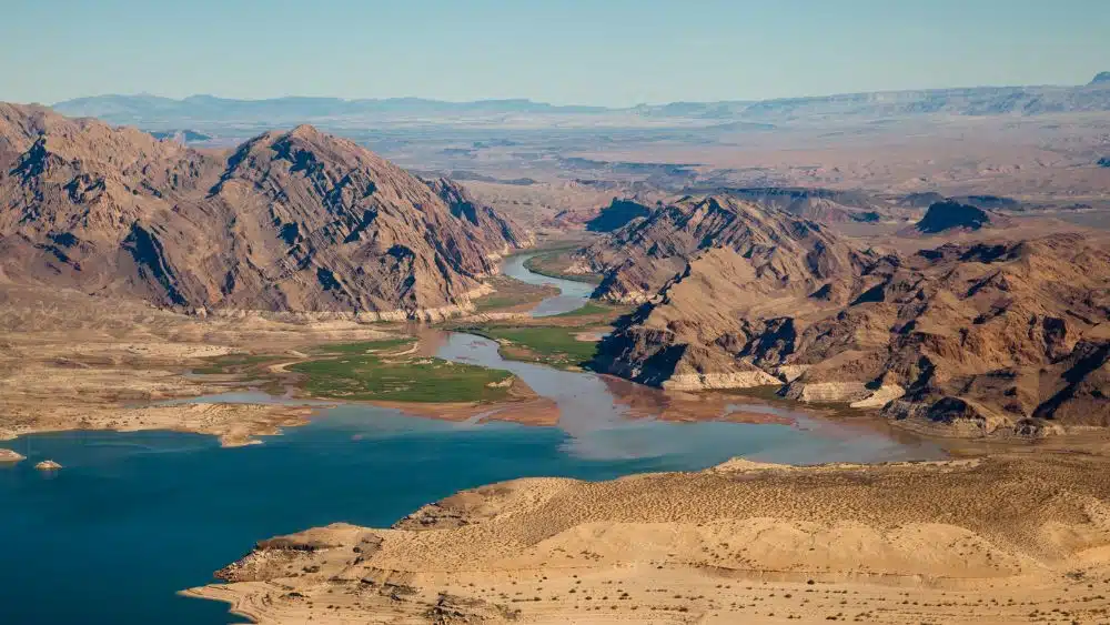 Aerial view ofr a body of water leading into a rive that winds between mountains in a desert area.