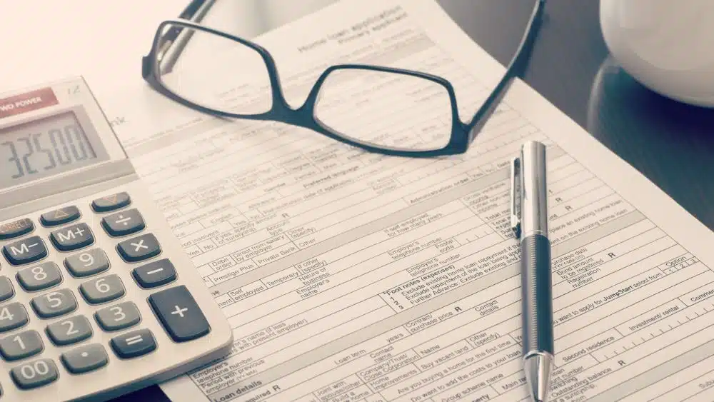 A paper home loan application with a calculator, pen, and glasses on top of it.