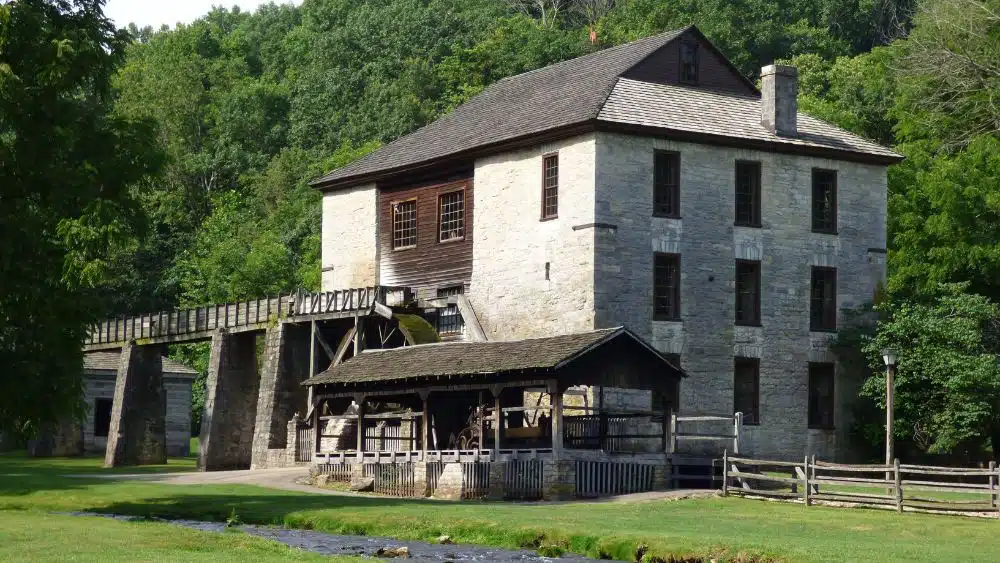 A large stone building with a bridge on one side and a small stable area in the front.