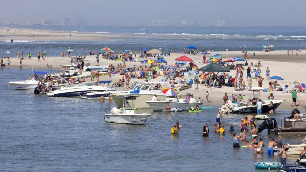 People hanging out at a busy beach with boats in the shallows.