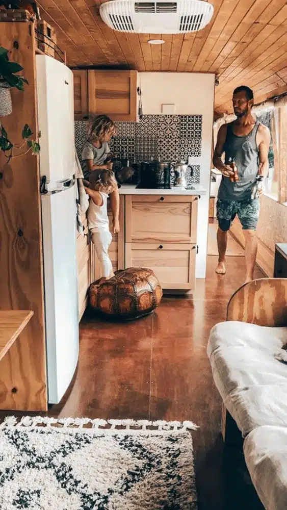 Two people standing in a tiny house kitchen that has wood accents and a black and white patterned backsplash.