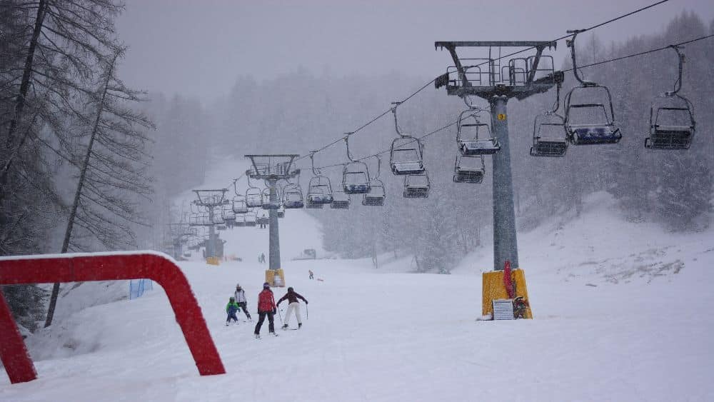 Ski lift with a few skiers on the ground during a snowstorm.