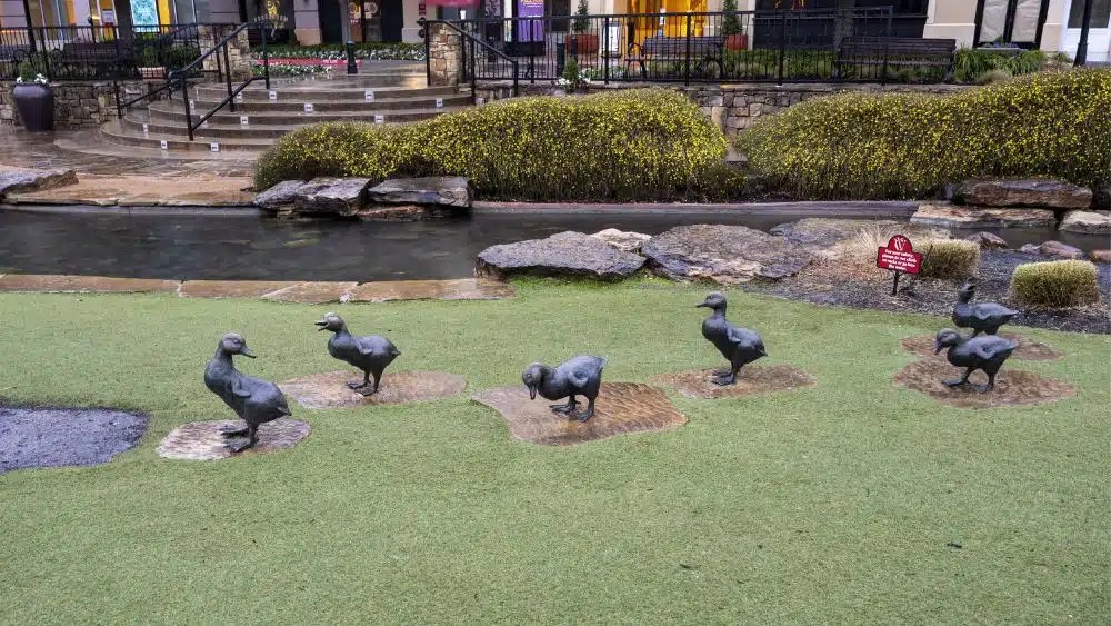 Small duck statues in a grassy area in a shopping center.