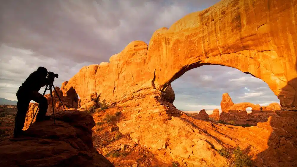 Person taking a picture of an arch formed from red rock.