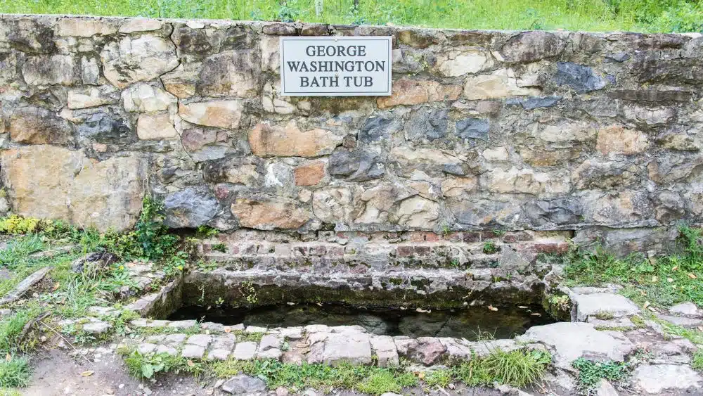 Rectangle cutout in the stone ground filled with water, with a sign that reads "George Washington Bathtub."