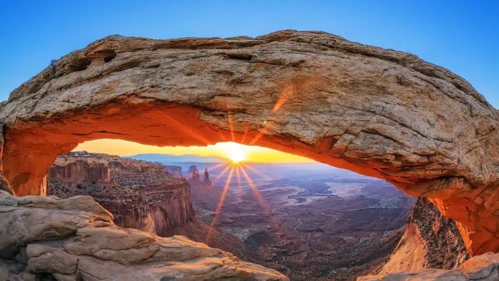 Sunset through a stone arch atop a canyon.