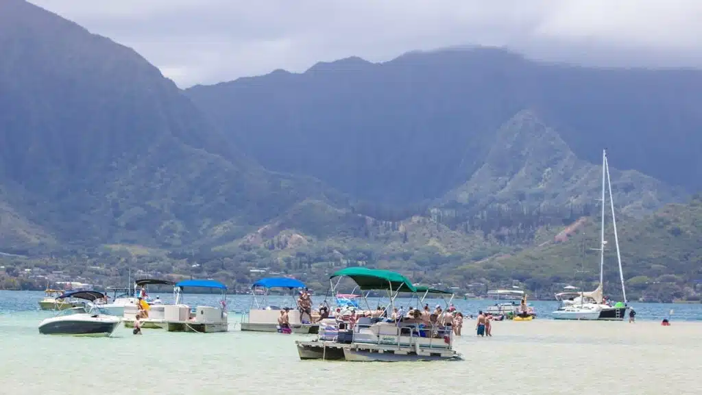 View of Kaneohe beach with mountains in the background and boats and swimmers in the foreground