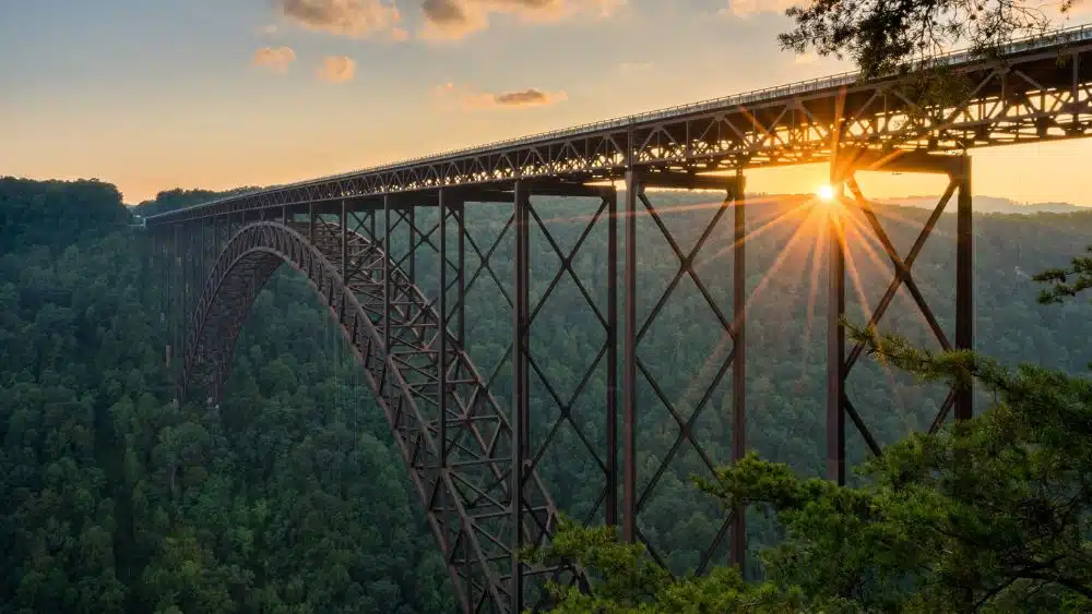 Long iron bridge spanning the distance of a mountain valley covered in a dense forest.